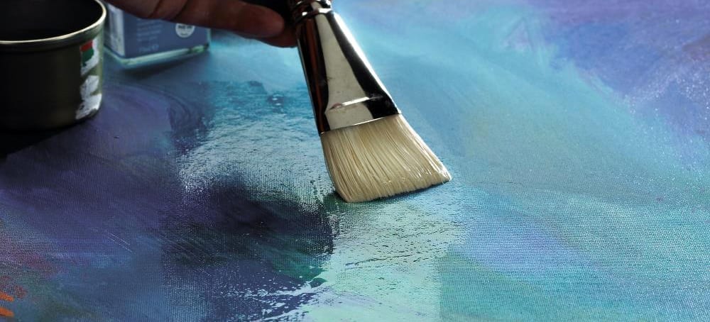 Paintbrush putting varnish on a finished painting